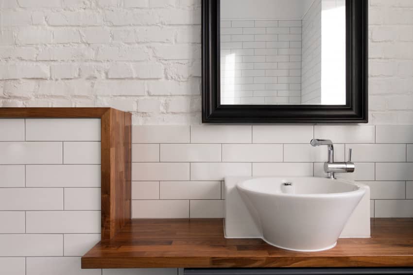 Bathroom vanity area with butcher block countertop, sink, tile backsplash, and mirror