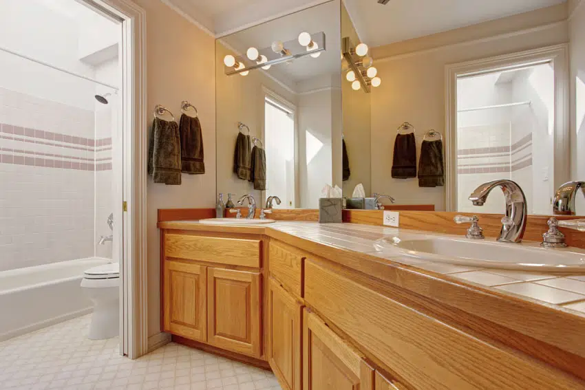 Bathroom vanity with honey oak cabinets, tile countertop, sink, faucet, and mirror