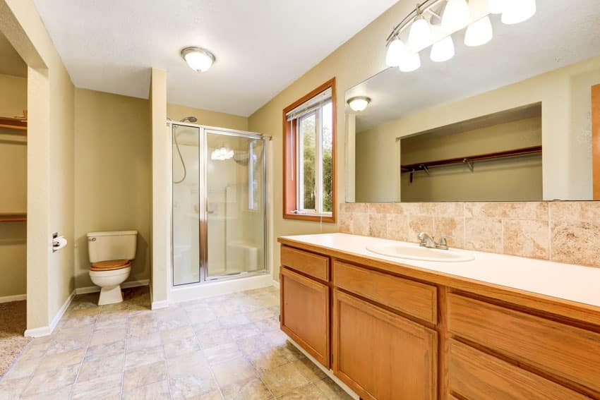 Bathroom with honey oak cabinet, vanity mirror, countertop, shower area, toilet, and windows