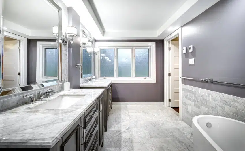 Bathroom with marble floor and countertops, grey wall, windows, and sconce lights