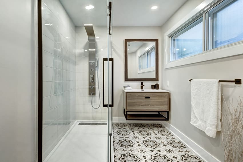 Bathroom with pattern vinyl floor sheets, floating vanity, glass door, shower area, modern showerhead, mirror, and windows