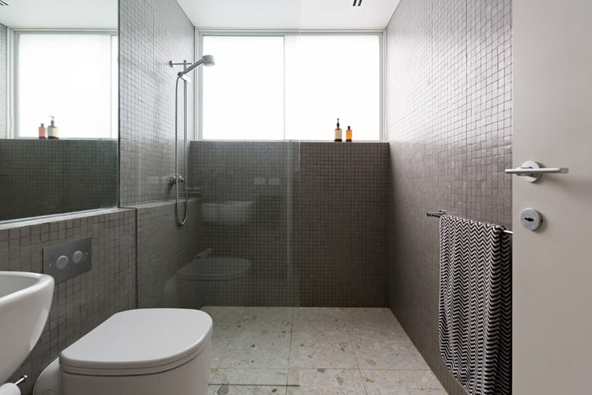 Bathroom with terrazzo flooring, glass divider, shower, window, toilet, and mirror