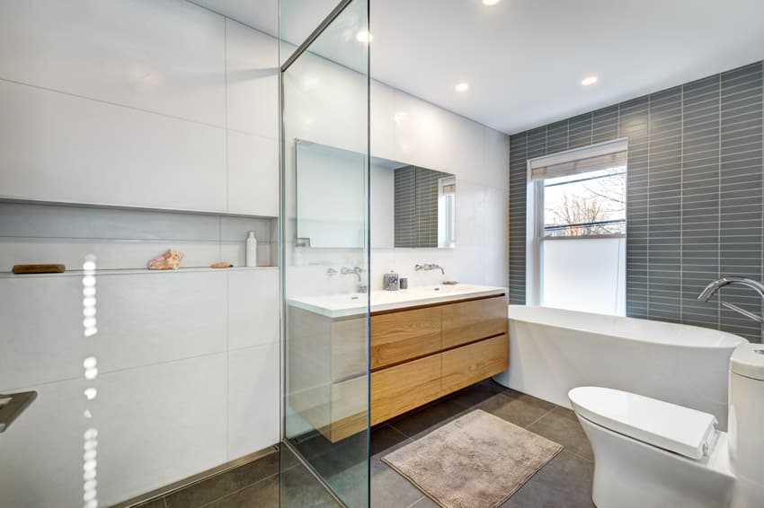 Bathroom with tub, toilet, glass divider, honey oak cabinets, mirror, and window