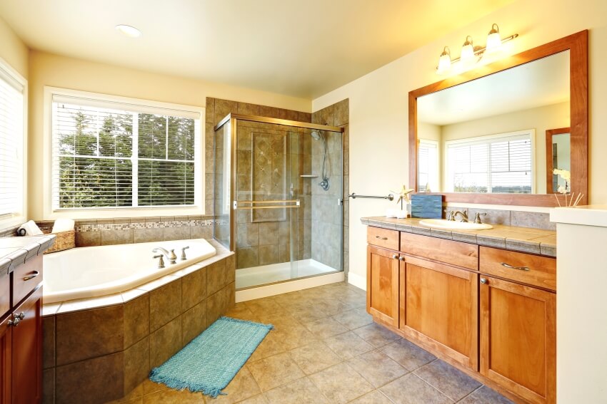 Bathroom with two vanity cabinets, glass walk-in shower and grey brown marble clad corner bathtub
