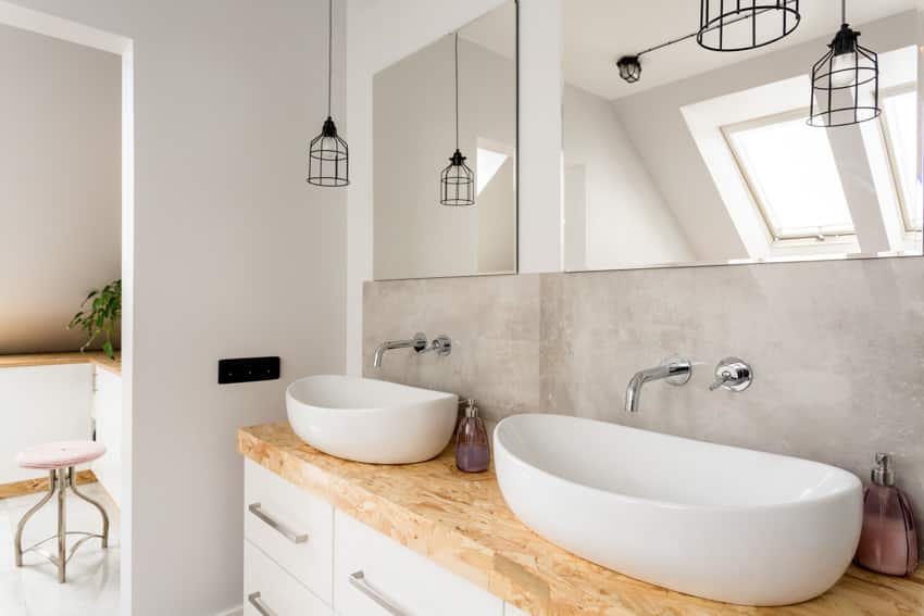 Bathroom with wood butcher block countertop, mirror, sinks, faucets, and hanging lights