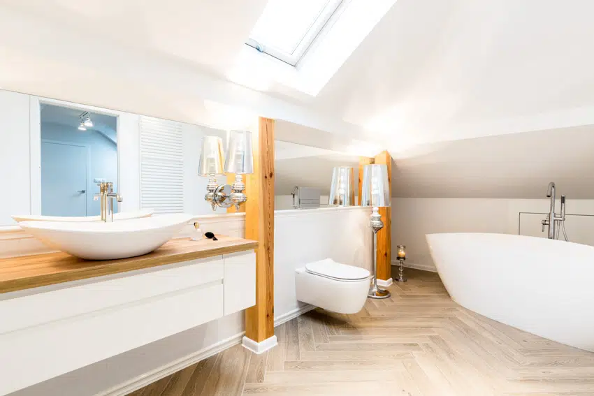 Bathroom with wood floor, butcher block countertop, mirror, drawers, tub, toilet, and skylight window