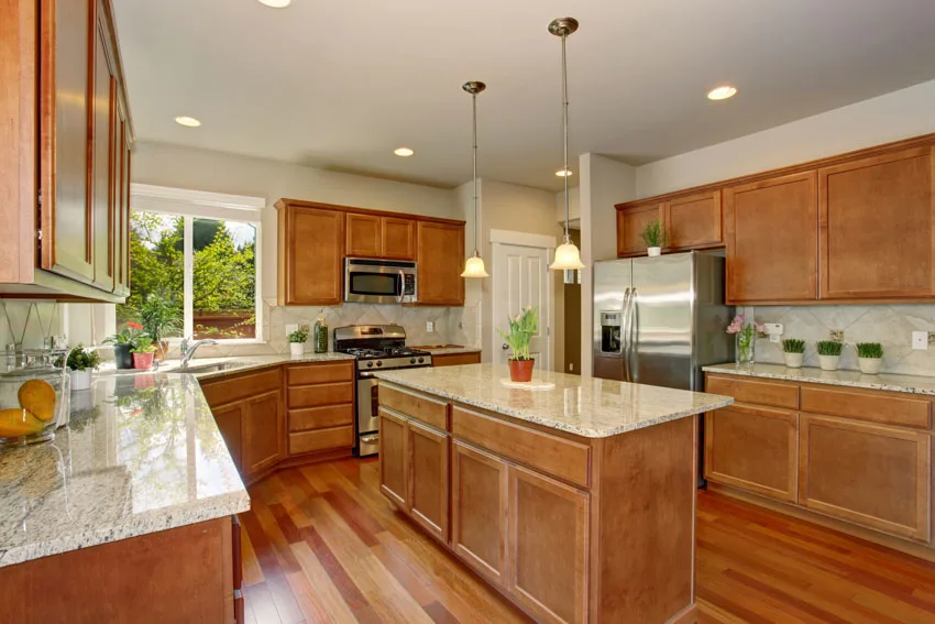 Beautiful kitchen with wood flooring, stained cabinets, island, countertops, backsplash, windows, and hanging lights