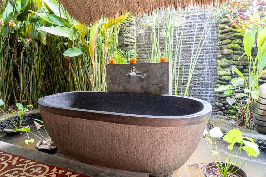 Beautiful outdoor bath with stone tub, faucet, and plants