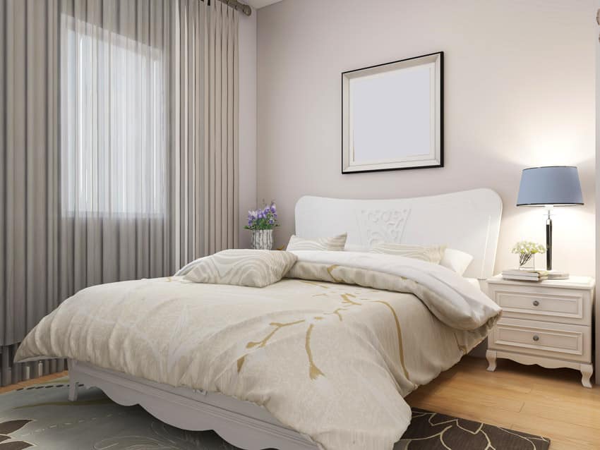 Bedroom with comforter, white headboard, nightstand, lamp, wood floor, and window curtain