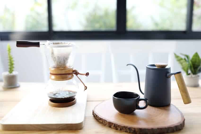 Black coffee cup with coffee dripper on acacia cutting board and a coffee drip brew pot on bamboo chopping board