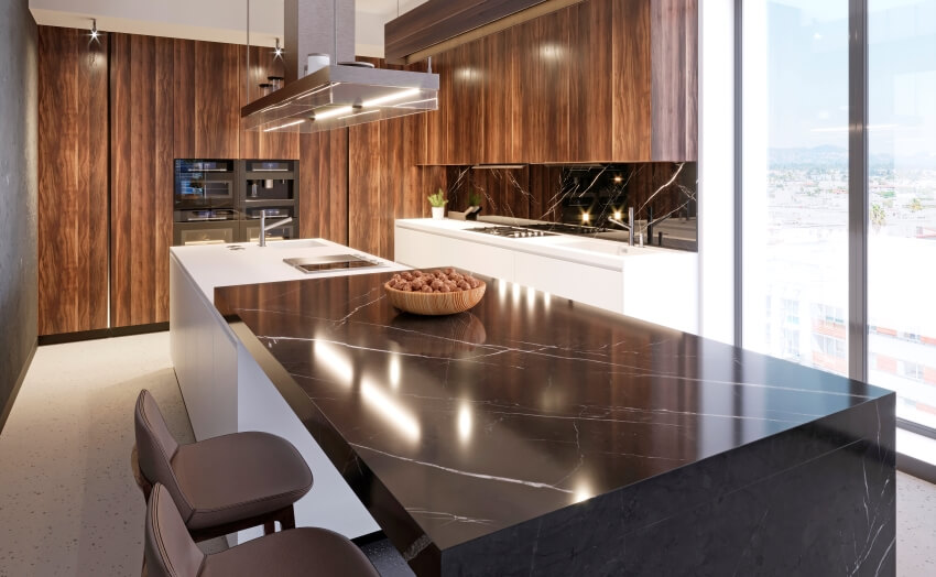 Black marble bar counter attached to an island in a kitchen with wooden cabinets