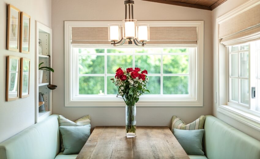 Breakfast nook with roses on rustic table, chandelier, and bench with pillows