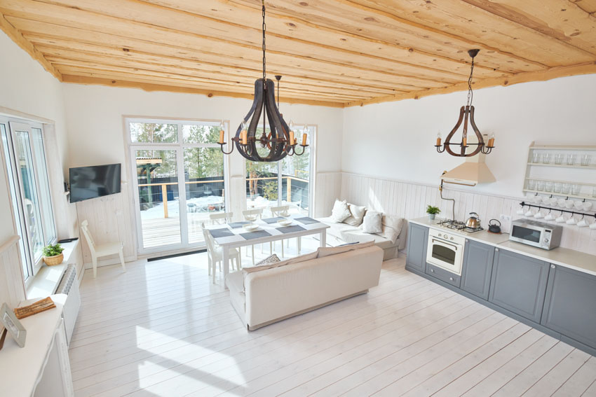 Kitchen with wood ceiling, plank floors, bluish gray cabinets and white couches