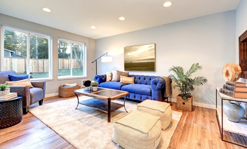 Bright living room with blue upholstered sofa, poufs, windows, and bigleaf maple floor