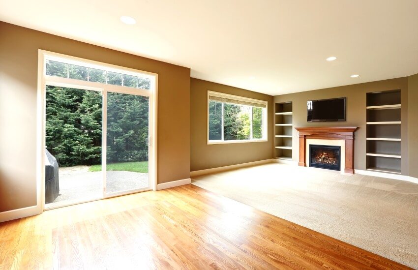 Brown living room interior with carpet to hardwood floor transition, fireplace, and bookshelves
