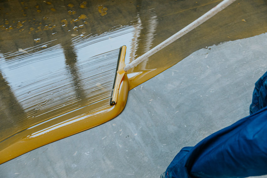 Contractor applying epoxy coating on concrete floor