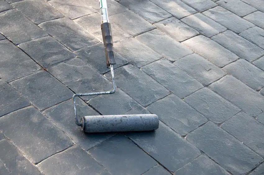 Contractor sealing concrete driveway with roller brush