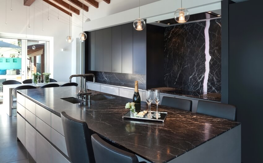 Dark kitchen with vaulted ceiling, pendant lights, and large island with black marble countertop