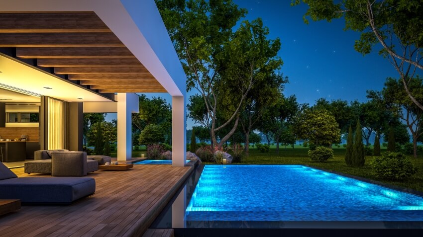Deck with ceiling beams, and a pool LED lights of a house with beautiful landscaping on background