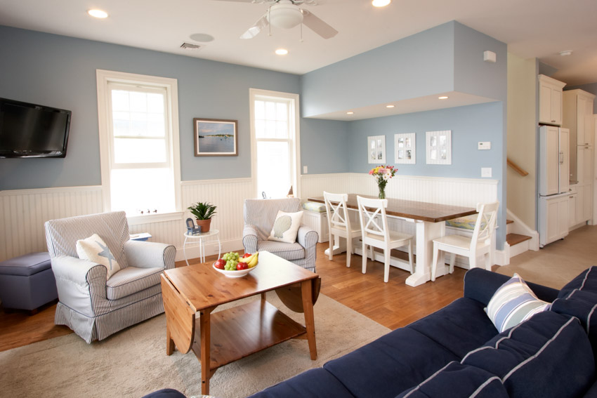 Dining and living room combined with wainscoting, blue wall, table, chairs, nook, couch, and windows