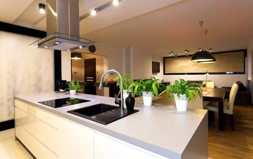 Dining area and kitchen with pendant lights, and island with plants, sink and cooktop on grey countertop
