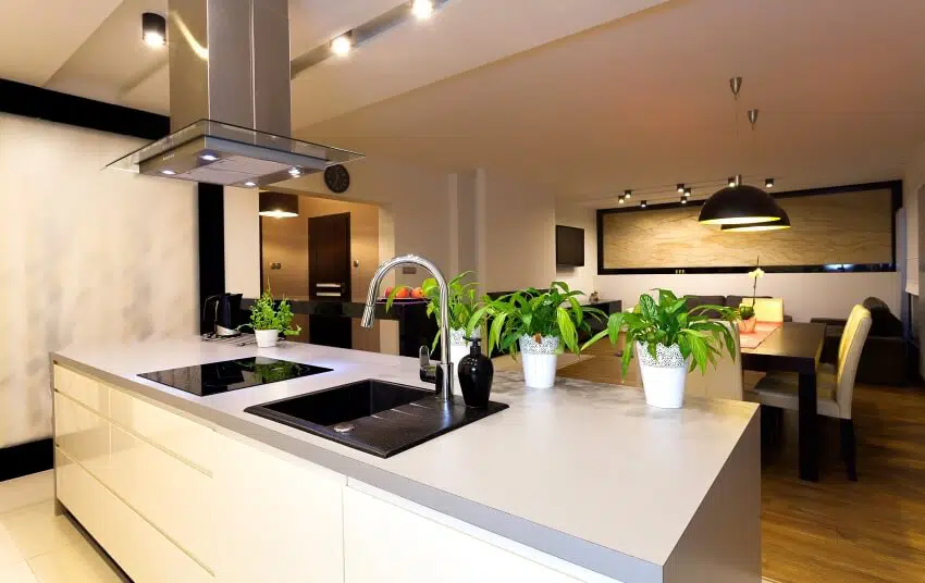 Dining area and kitchen with pendant lights, and island with plants, sink and cooktop on grey countertop