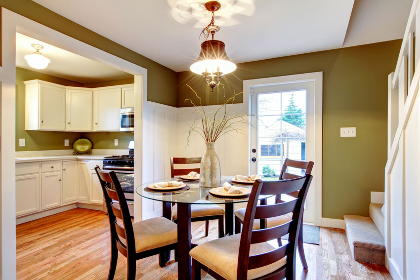 Dining room near kitchen with green wall, wainscoting, table, chairs, and ceiling light
