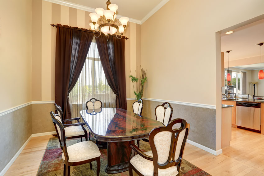 Dining room with window curtain, table, chairs, wainscoting, wood flooring, cream walls, and chandelier