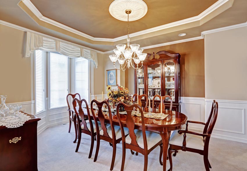 Dining room with wood chairs, table, glass cabinet, wainscoting, and windows