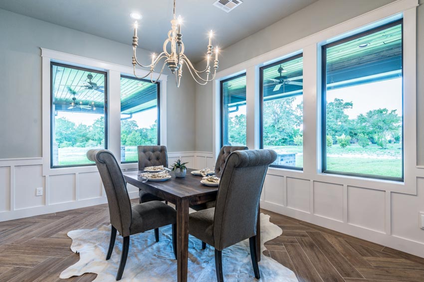 Dining room with wood floor, windows, hanging light, wainscoting, table, and chairs