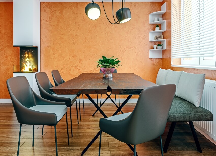 Dining room with wooden table, chairs, bench, orange wall, and a fireplace