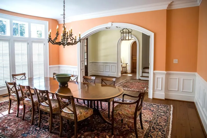 Arched entruway with white trimming, windows with shutters and table with green bown on top
