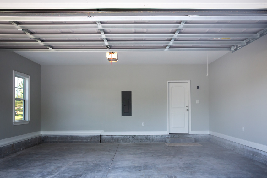 Empty garage with door, white wall, window, and concrete overlay