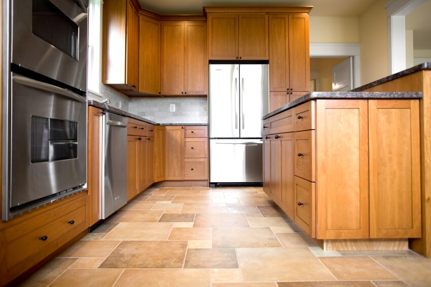 Empty kitchen with stainless steel appliances, wooden cabinets, and limestone floor