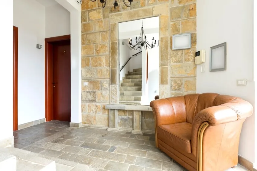 Entrance hall with mirror, brown leather armchair, and limestone wall and floor
