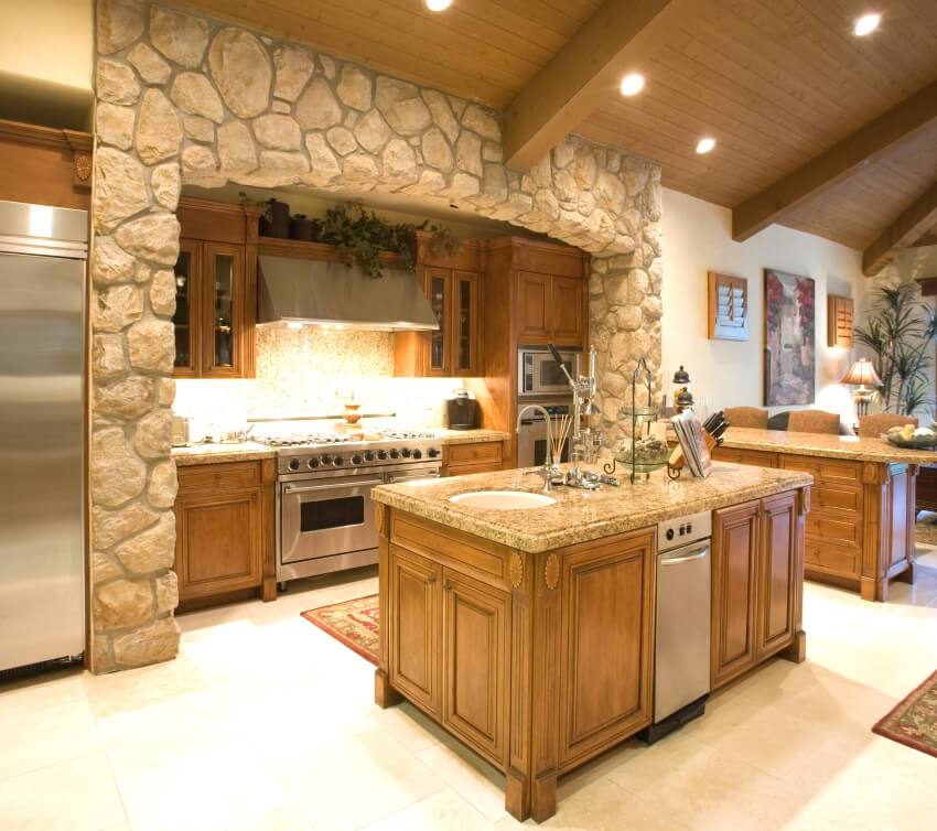 Exposed stone kitchen surround with wooden ceiling, granite countertops, and limestone tile floor