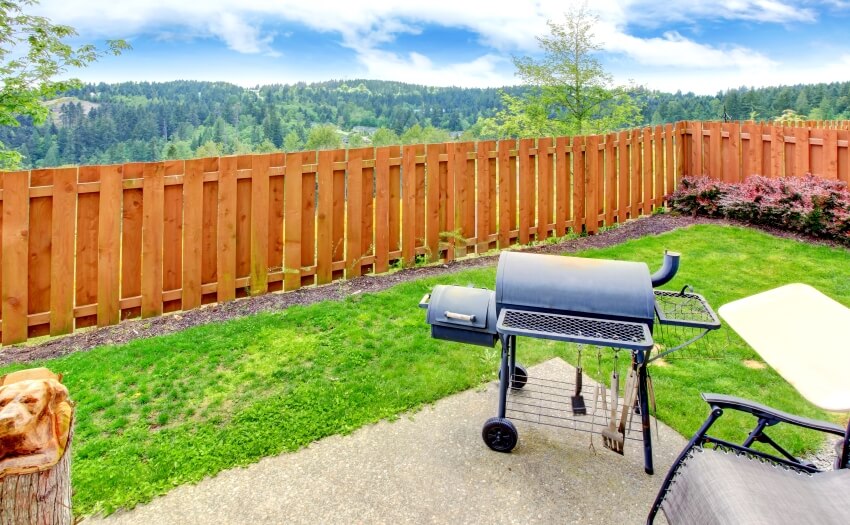 Fenced backyard with a forest view concrete patio and barbecue area