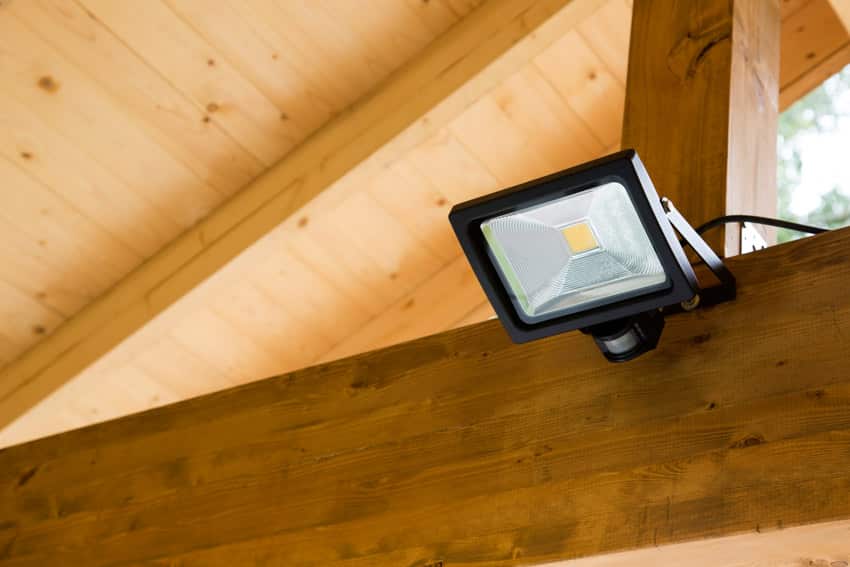 Flood light with small motion sensor installed on top of wood beam