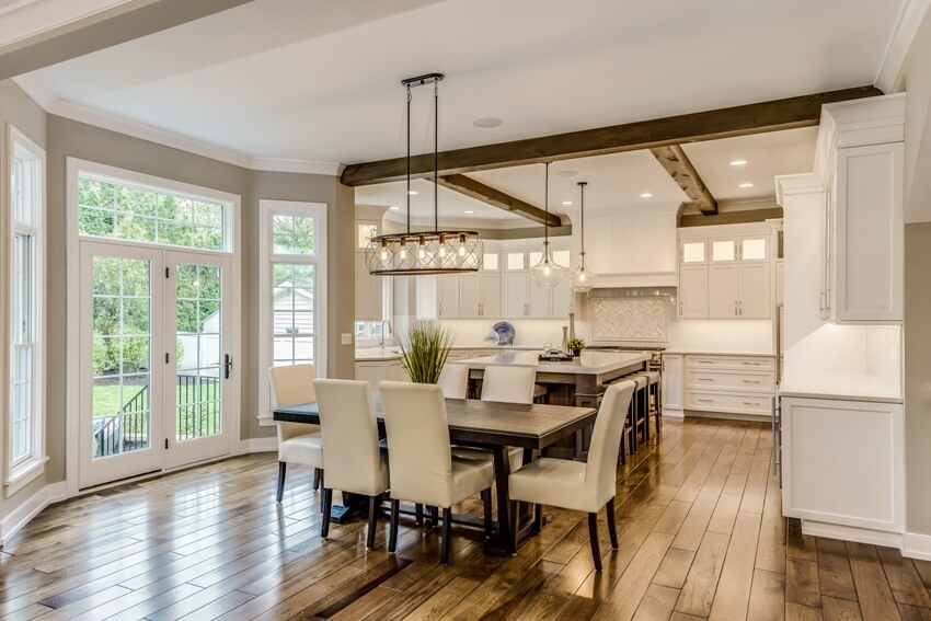 Fresh looking kitchen design with wood beams on ceiling two pendant lights hang over island and engineered wood flooring