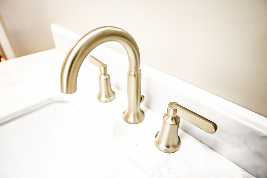 Gold finished faucet with controls on top of a bathroom sink