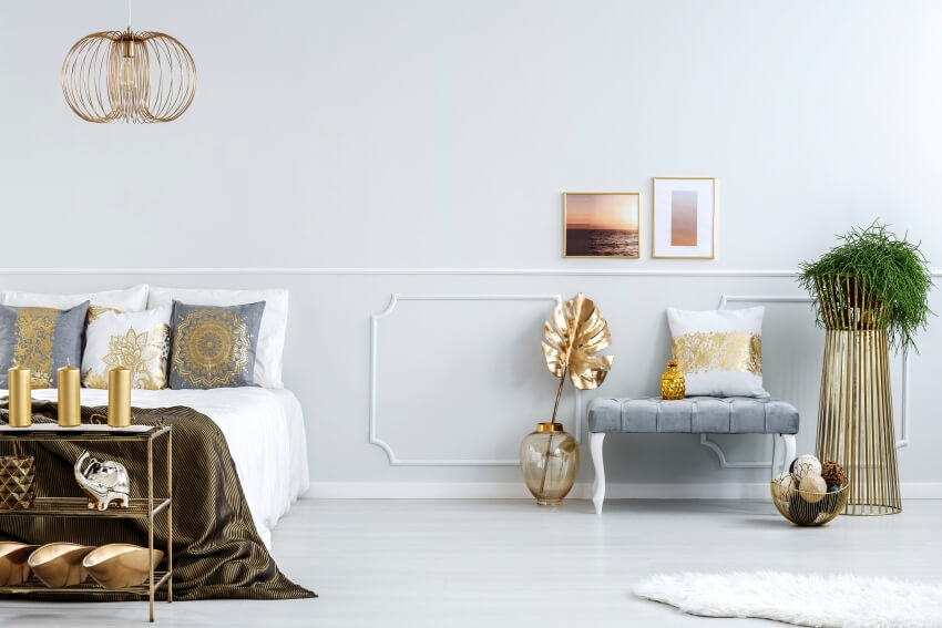 Golden decorations in bedroom interior with double bed, bench, pendant light, and plant in a pot
