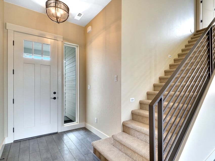 Hallway with beige walls, staircase with black metal railing, and semi-flush lighting