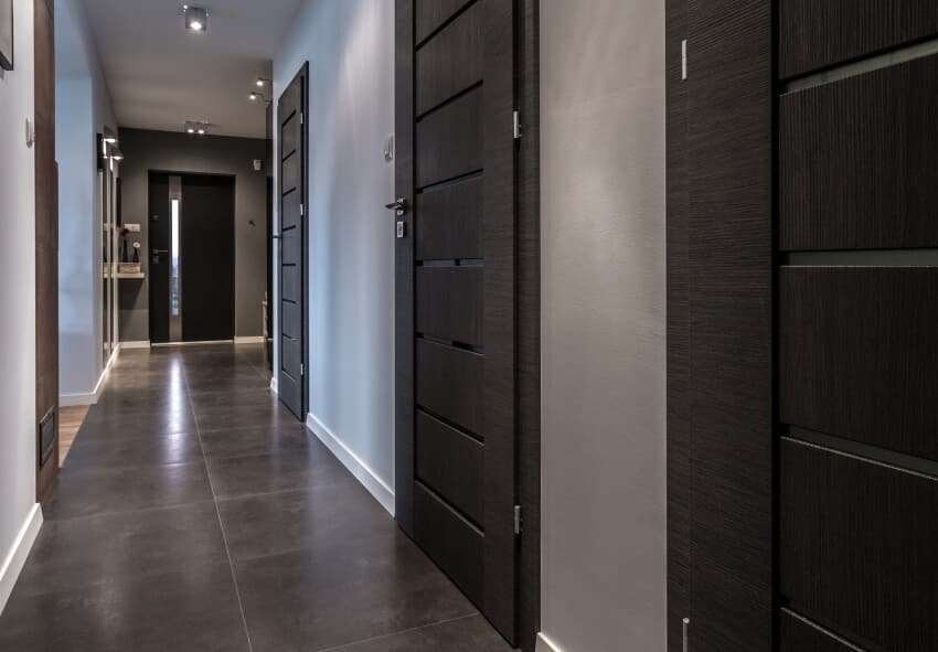 Hallway with black tile floor, grey walls, and ceiling and wall lights