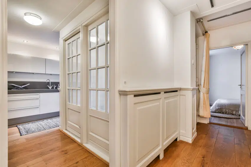 Hallway with white wall, wainscoting, doors, and wood floors