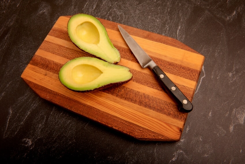 Halved avocado with knife on acacia cutting board