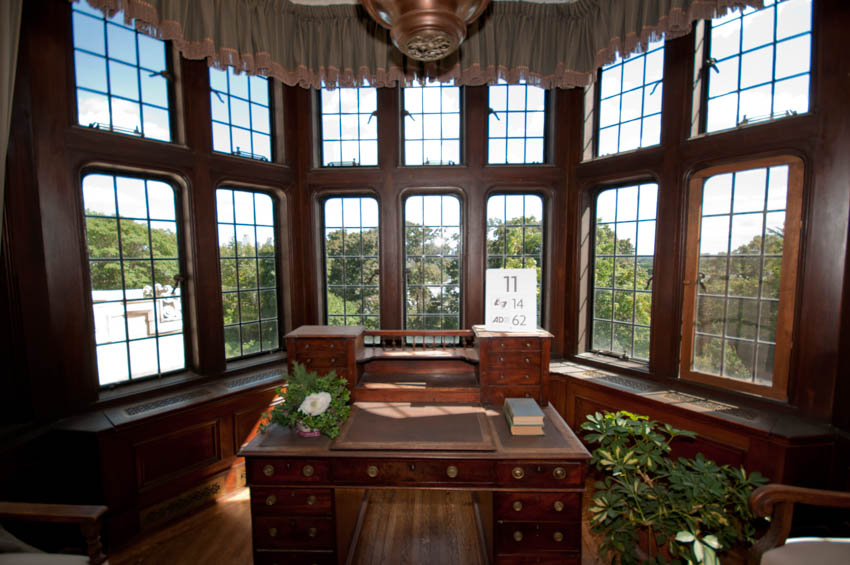 Home office with bay window, wood desk, ceiling light, and potted plant