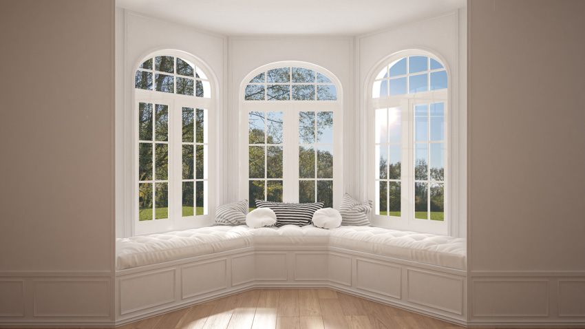 House interior with bay window, nook, cushioned seats, pillows, and wood floor
