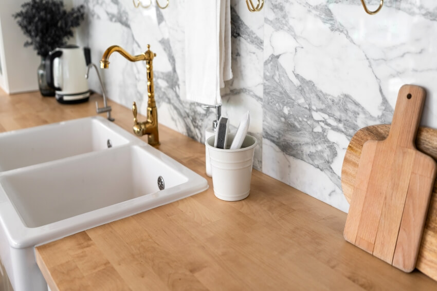 Kitchen with wood top, marble backsplash, and white ceramic sink with gold faucet