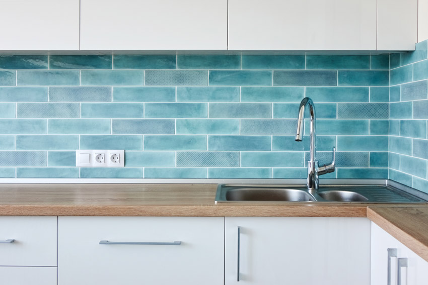 Kitchen with blue green tile backsplash, countertops that look like wood, and metal sink