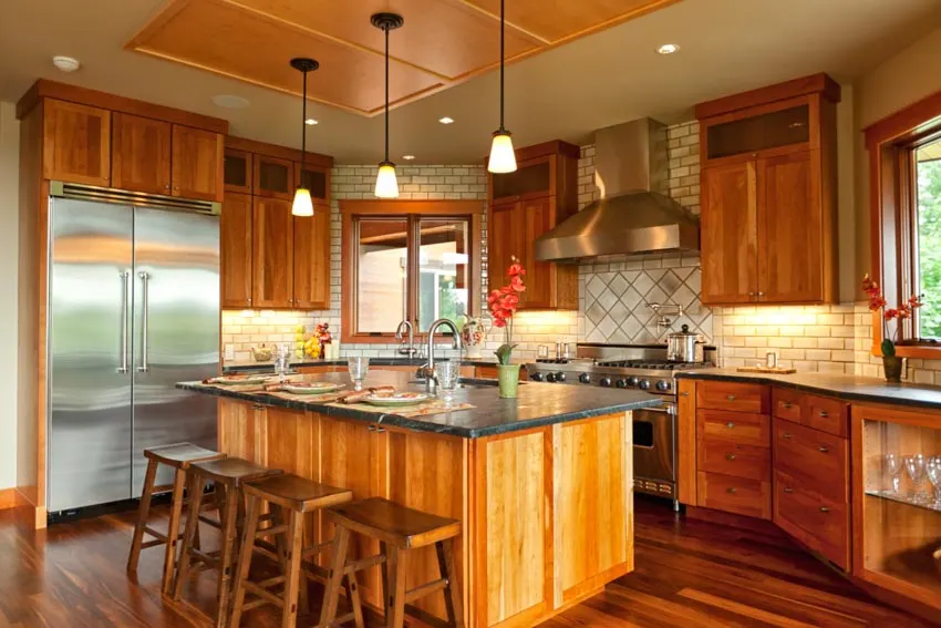 Kitchen with center island, chairs, stained cabinets, wood flooring, backsplash, range hood, and pendant lights